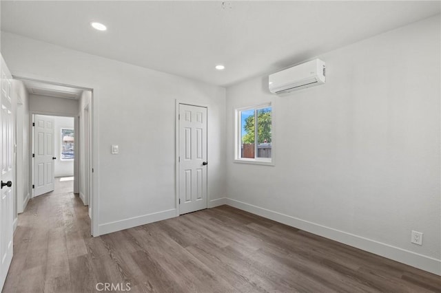 unfurnished bedroom featuring an AC wall unit, baseboards, recessed lighting, wood finished floors, and a closet