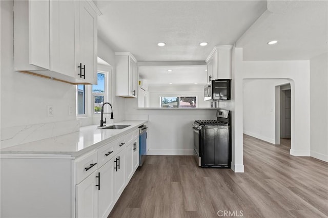 kitchen featuring recessed lighting, stainless steel appliances, wood finished floors, a sink, and white cabinetry