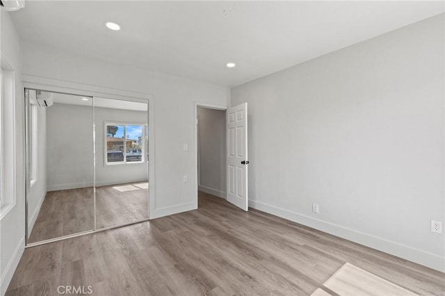 unfurnished bedroom with a wall mounted AC, baseboards, wood finished floors, and recessed lighting