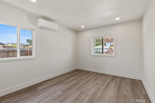 empty room with an AC wall unit, baseboards, light wood finished floors, and recessed lighting