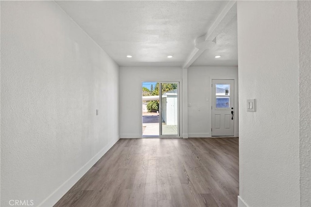 spare room featuring a textured wall, baseboards, and wood finished floors