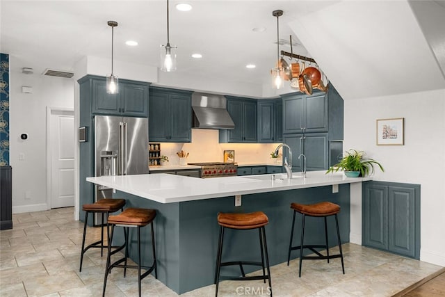 kitchen featuring a kitchen breakfast bar, light countertops, high end fridge, hanging light fixtures, and wall chimney range hood