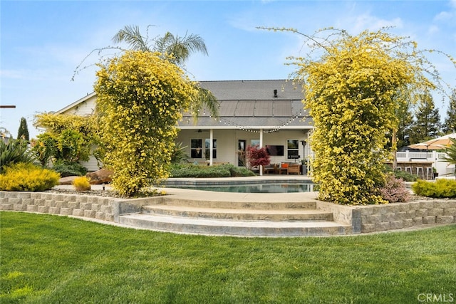 rear view of property with a lawn, an outdoor pool, a patio, and roof mounted solar panels