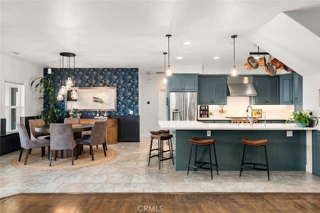 kitchen with high quality fridge, light countertops, a sink, wall chimney exhaust hood, and a kitchen breakfast bar