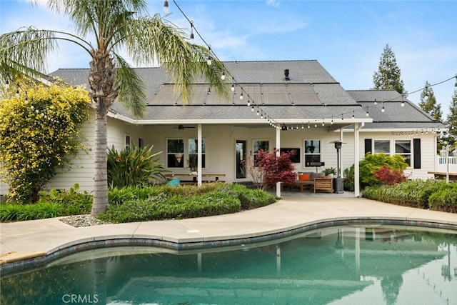 rear view of house with roof mounted solar panels, ceiling fan, an outdoor living space, roof with shingles, and a patio area