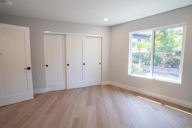 unfurnished bedroom with a closet, light wood finished floors, and baseboards