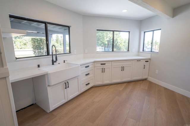 kitchen featuring white cabinets, a sink, light wood-style floors, and a healthy amount of sunlight