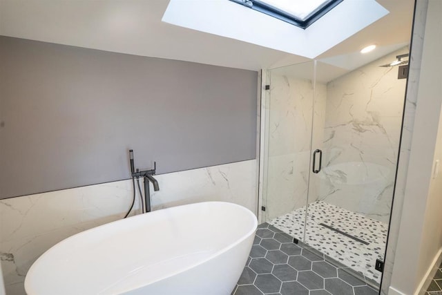 bathroom with recessed lighting, a freestanding bath, a marble finish shower, tile walls, and a skylight