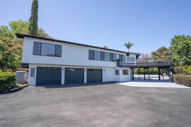 view of front of property with central air condition unit, driveway, a garage, a wooden deck, and stucco siding