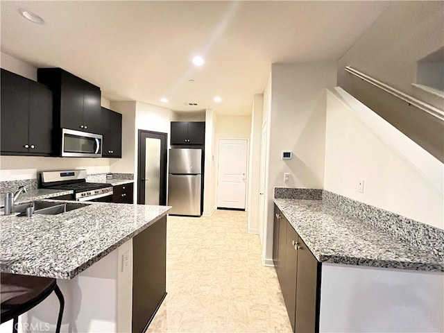 kitchen with a sink, dark cabinetry, appliances with stainless steel finishes, and a peninsula