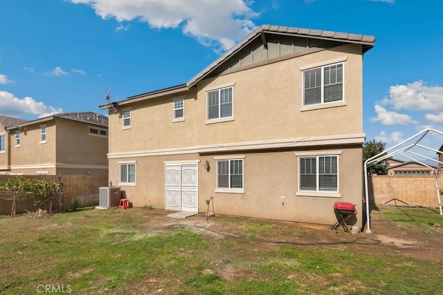back of property featuring stucco siding, a yard, central AC unit, and fence