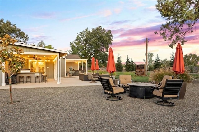 yard at dusk with a patio, an outdoor living space with a fire pit, outdoor dry bar, and a ceiling fan