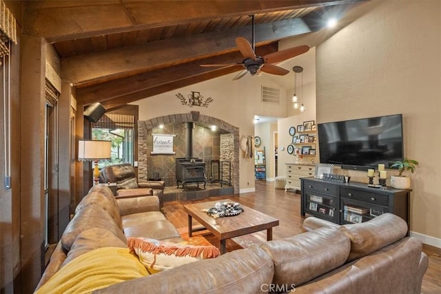living room featuring visible vents, vaulted ceiling with beams, ceiling fan, a wood stove, and wood finished floors