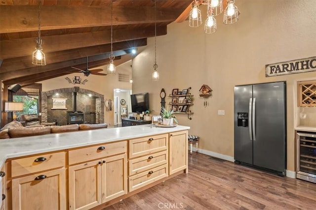 kitchen featuring light brown cabinets, beverage cooler, open floor plan, a wood stove, and stainless steel fridge