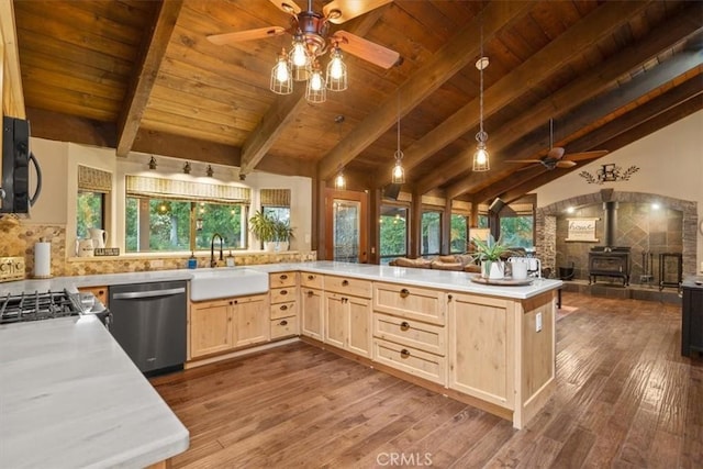 kitchen with a wood stove, a sink, light brown cabinetry, ceiling fan, and stainless steel dishwasher