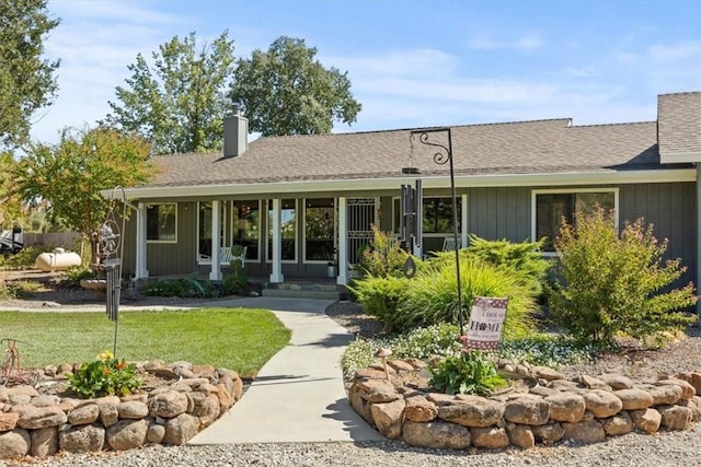 exterior space featuring covered porch, a chimney, a front yard, and a shingled roof