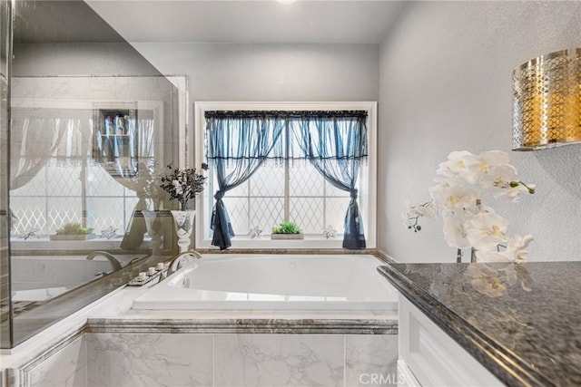 bathroom with vanity, a textured wall, and a bath