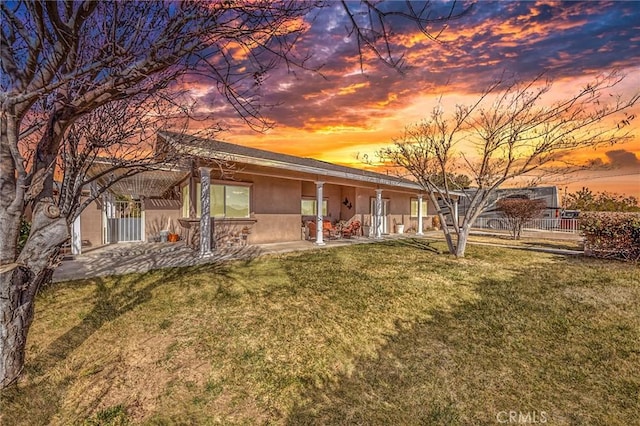 back of house at dusk featuring a lawn, stucco siding, and a patio