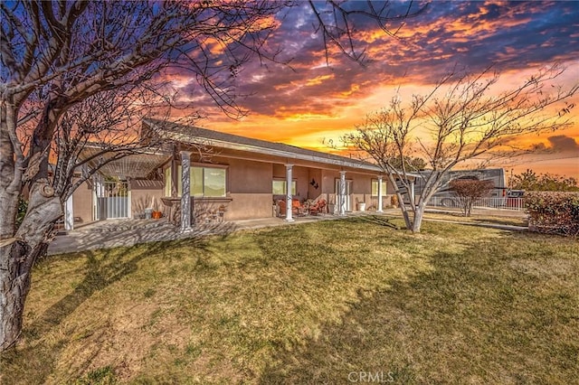 6116 Panorama St, Joshua Tree, CA 92252 - back of property at dusk with stucco siding, a lawn, and a patio area