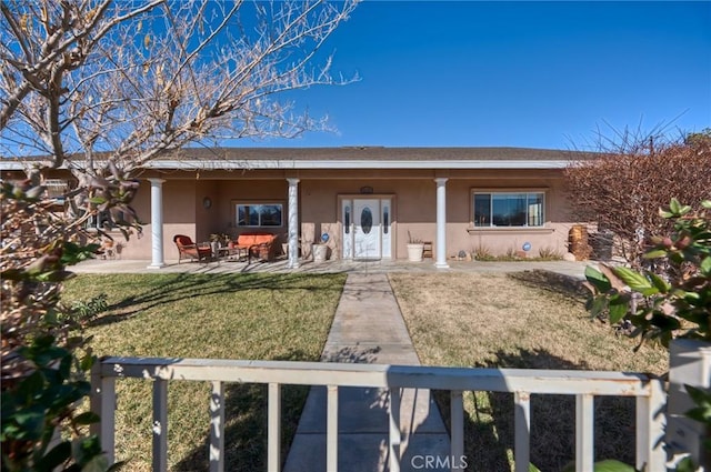 rear view of house featuring a lawn and stucco siding