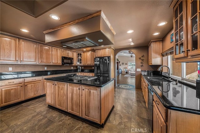 kitchen featuring a sink, arched walkways, a center island, dark stone counters, and black appliances