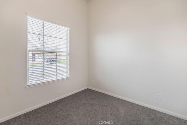 unfurnished room with baseboards and dark carpet