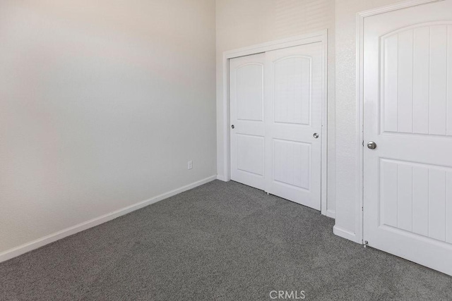 unfurnished bedroom featuring dark colored carpet, a closet, and baseboards