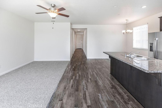 kitchen featuring dark wood-type flooring, baseboards, pendant lighting, ceiling fan with notable chandelier, and a sink