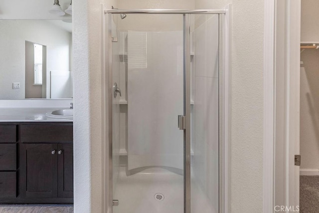 full bath with vanity, a textured wall, and a stall shower