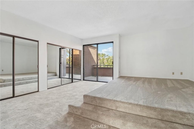 unfurnished bedroom featuring access to exterior, two closets, carpet floors, and a textured ceiling