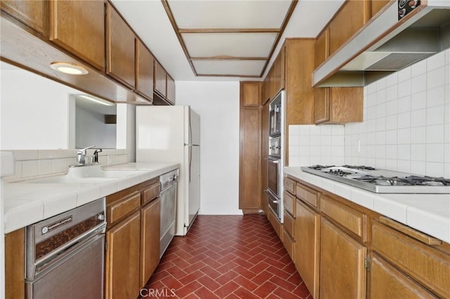 kitchen featuring tile countertops, a sink, decorative backsplash, stainless steel appliances, and under cabinet range hood