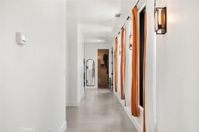 corridor with baseboards, visible vents, and concrete floors