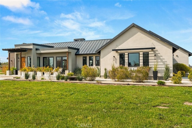 rear view of house with a lawn, metal roof, a standing seam roof, and stucco siding