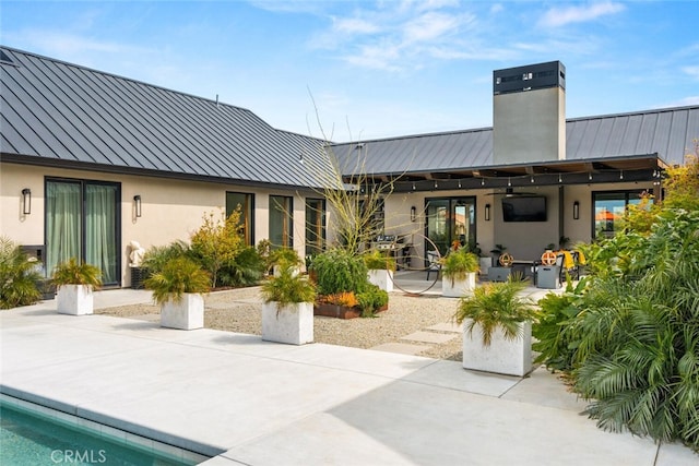 rear view of house featuring a standing seam roof, metal roof, a patio, and a chimney