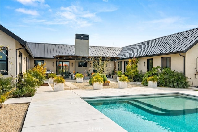 rear view of property featuring a patio, metal roof, a standing seam roof, and a chimney