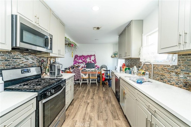 kitchen featuring light countertops, tasteful backsplash, stainless steel appliances, visible vents, and light wood-style flooring