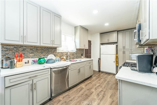 kitchen featuring light countertops, a sink, backsplash, appliances with stainless steel finishes, and light wood-style flooring