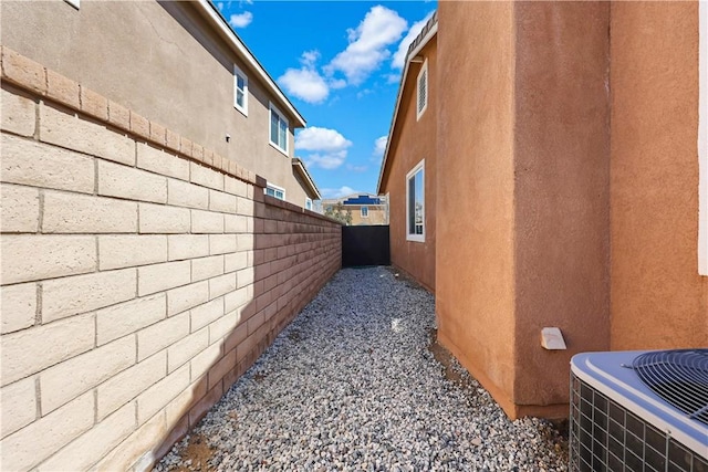 view of side of property with a fenced backyard, central AC, and stucco siding