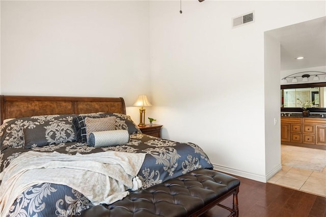 bedroom featuring wood finished floors, visible vents, a towering ceiling, and baseboards