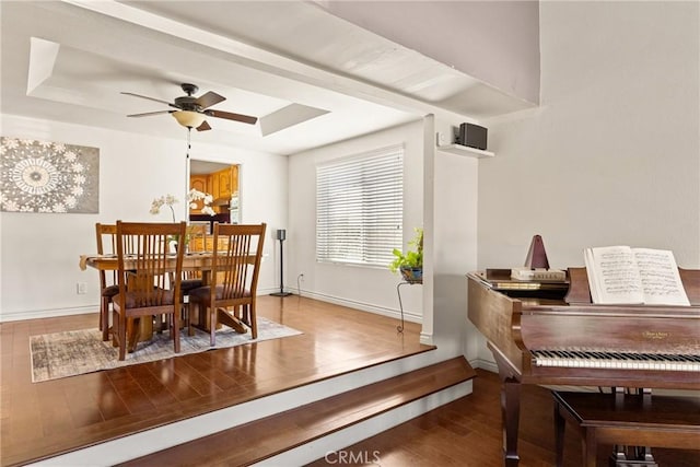 dining area with a tray ceiling, wood finished floors, a ceiling fan, and baseboards