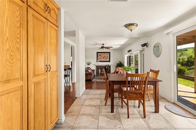 dining space with a warm lit fireplace, baseboards, and ceiling fan