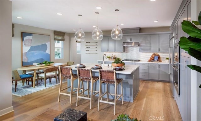 kitchen featuring backsplash, gray cabinetry, under cabinet range hood, light countertops, and gas cooktop