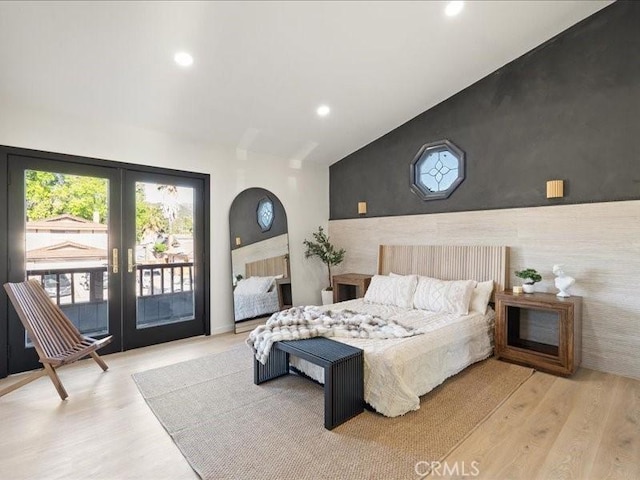 bedroom featuring access to exterior, an accent wall, lofted ceiling, and wood finished floors