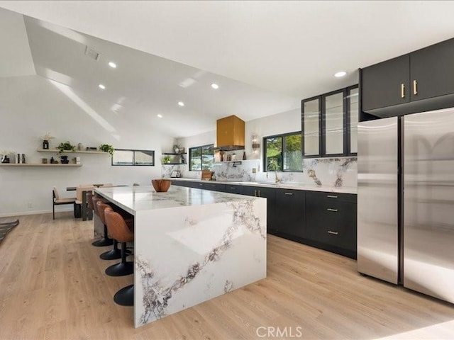 kitchen with dark cabinets, a center island, light wood-type flooring, and built in fridge