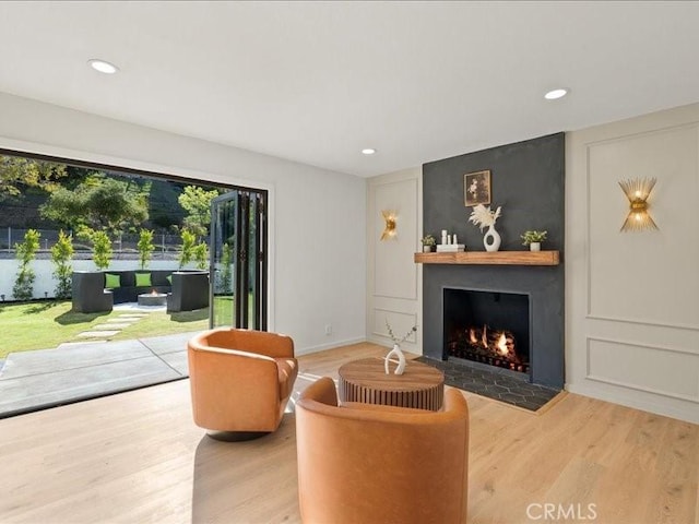 living area featuring wood finished floors, recessed lighting, a fireplace, a decorative wall, and baseboards