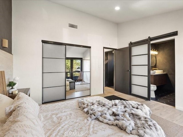 bedroom featuring visible vents, a barn door, recessed lighting, wood finished floors, and ensuite bath