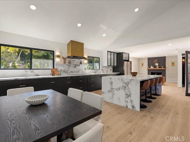 kitchen featuring a kitchen island, lofted ceiling, range hood, freestanding refrigerator, and dark cabinetry