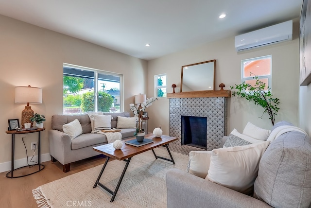 living room with a wall unit AC, baseboards, light wood finished floors, recessed lighting, and a fireplace