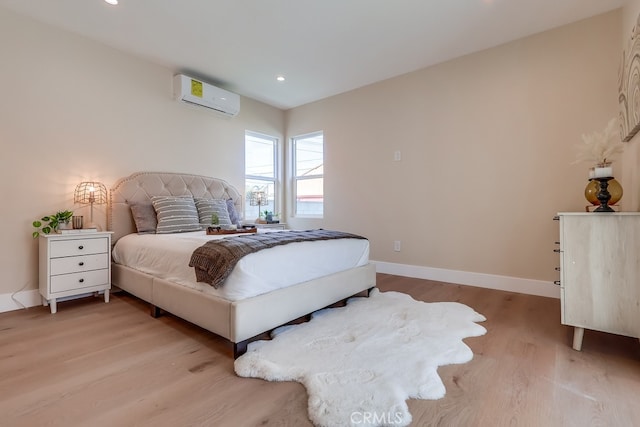 bedroom with a wall mounted air conditioner, baseboards, light wood-style flooring, and recessed lighting