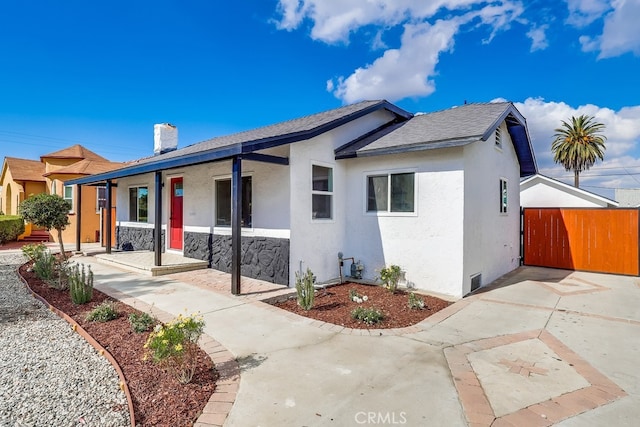 view of front of house featuring stucco siding, covered porch, a chimney, and fence